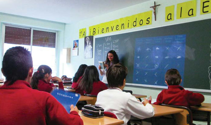 a teacher stands in front of her class with spanish symbolson a blackboard behind her